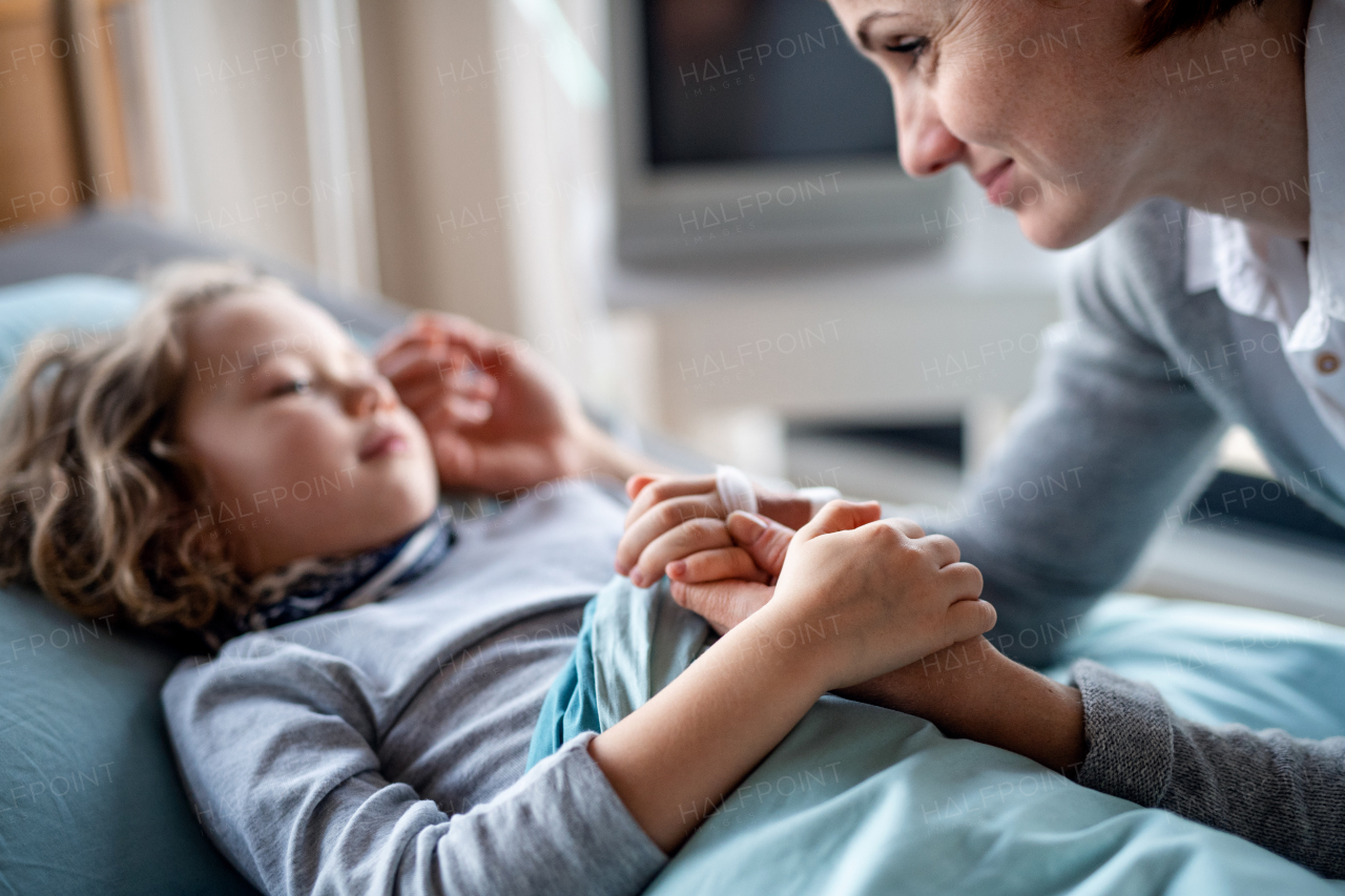 Caring mother visiting small girl daughter in bed in hospital, midsection.