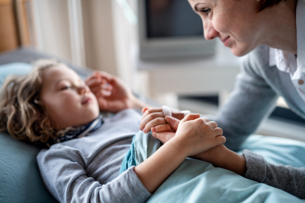 Caring mother visiting small girl daughter in bed in hospital, midsection.