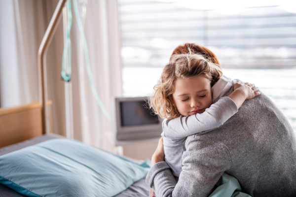 Caring mother visiting sleeping small girl daughter in hospital, hugging.