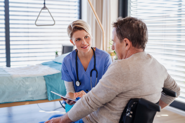 A healthcare worker and senior patient in wheelchair in hospital or at home, talking.