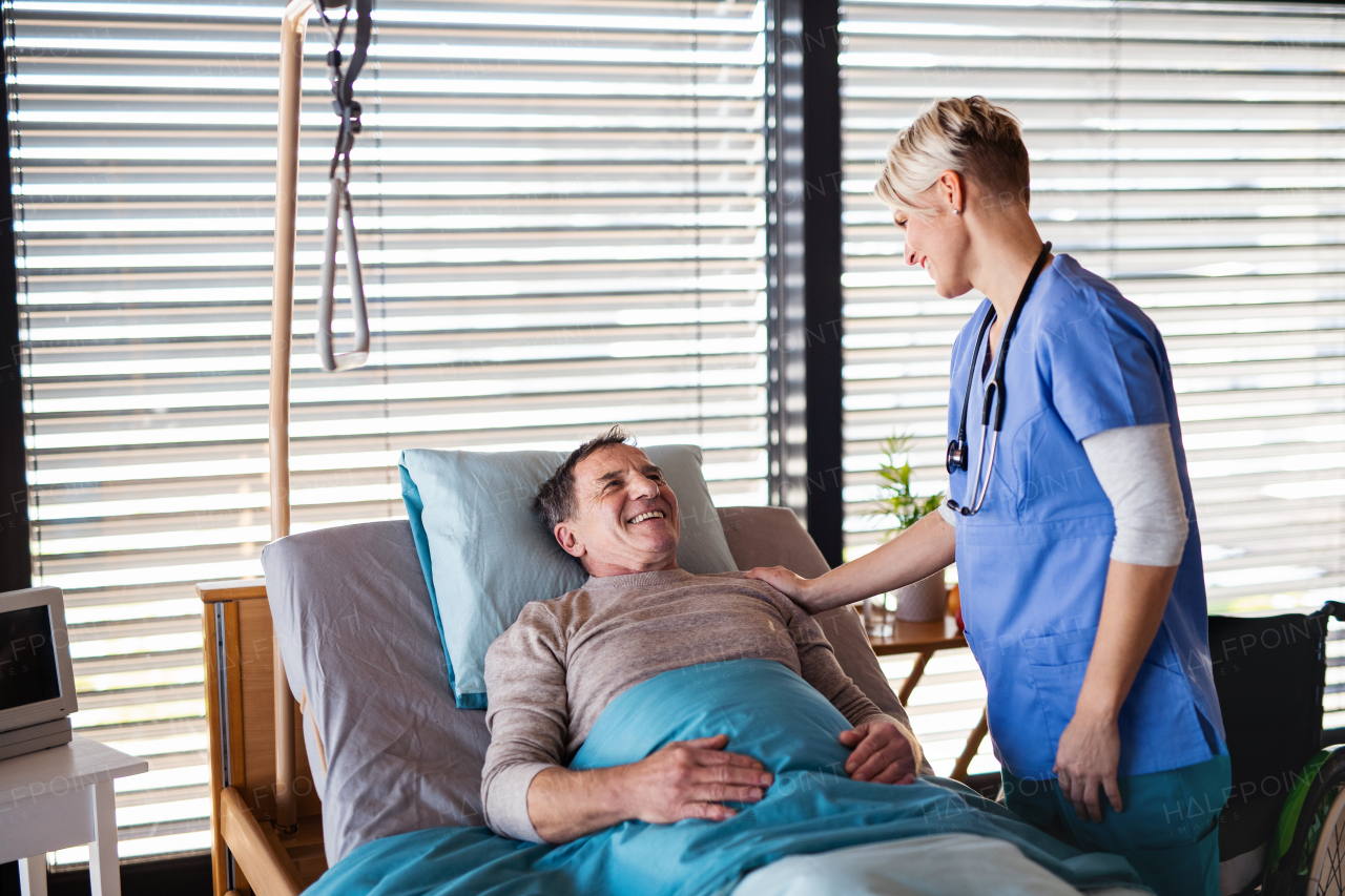 Friendly healthcare worker or nurse tallking to senior patient in bed in hospital.