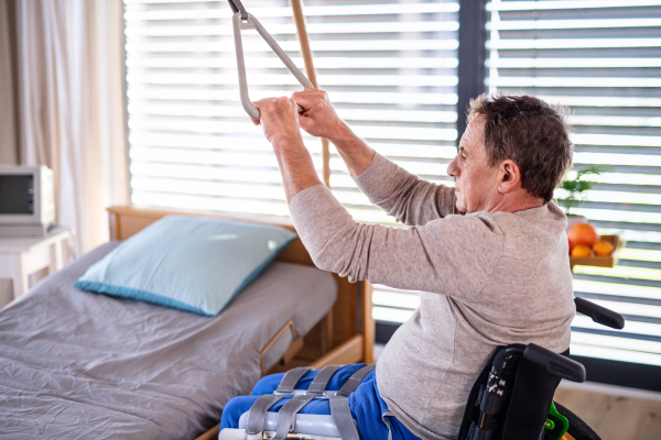 A man senior patient in wheelchair in hospital, holding onto a bed hanger.