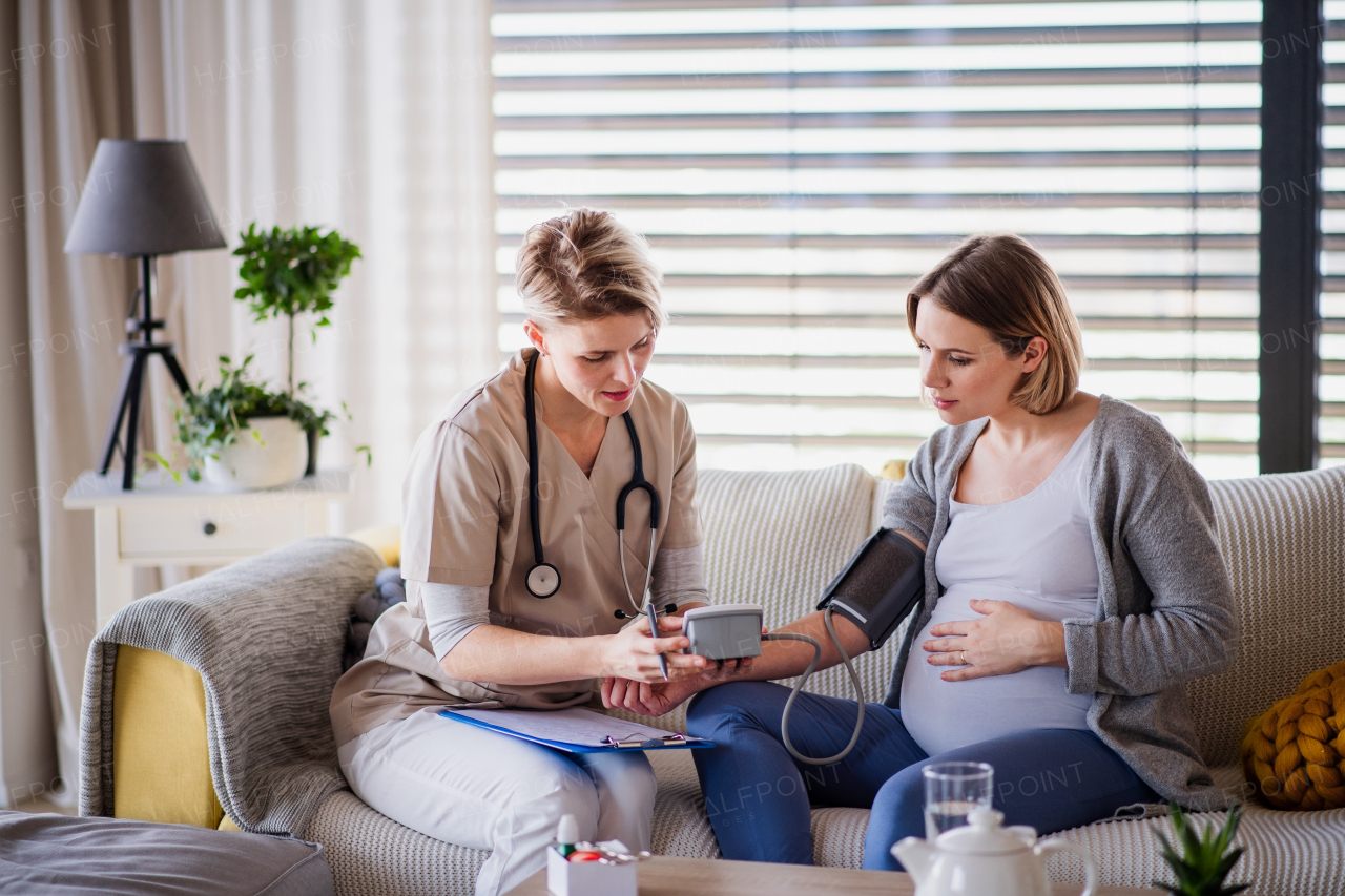 A healthcare worker examining pregnant woman indoors at home, checking blood pressure.