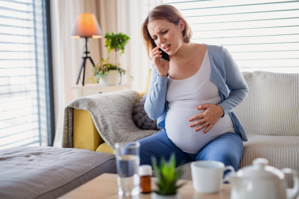 A portrait of pregnant woman in pain indoors at home, making emergency call.