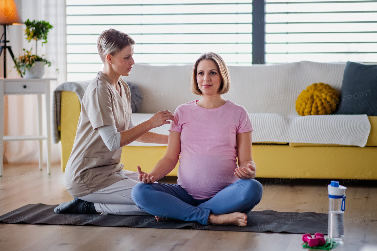 Contented pregnant woman doing yoga exercise with instructor at home.