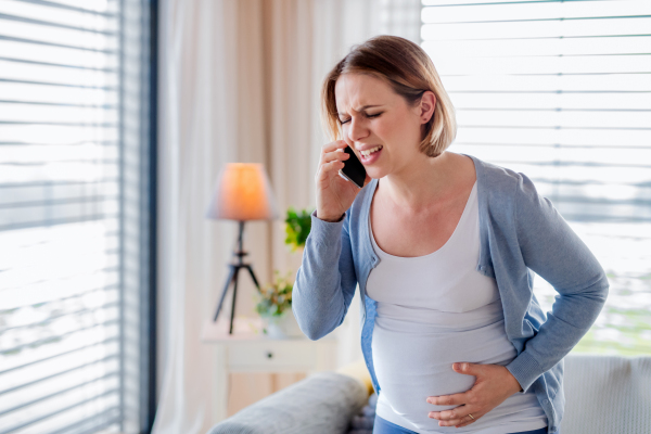 A portrait of pregnant woman in pain indoors at home, making emergency call.