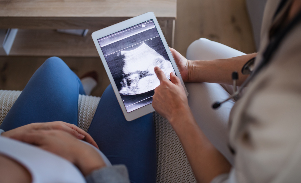 Unrecognizable healthcare worker with ultrasound on tablet and pregnant woman, top view.