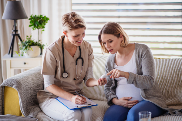 A healthcare worker examining pregnant woman indoors at home, checking sugar level.