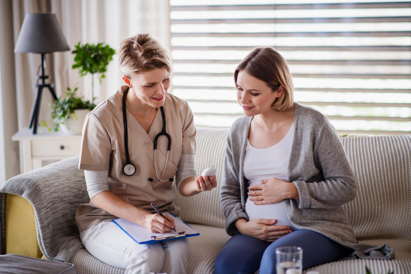 A healthcare worker examining pregnant woman indoors at home, checking sugar level.