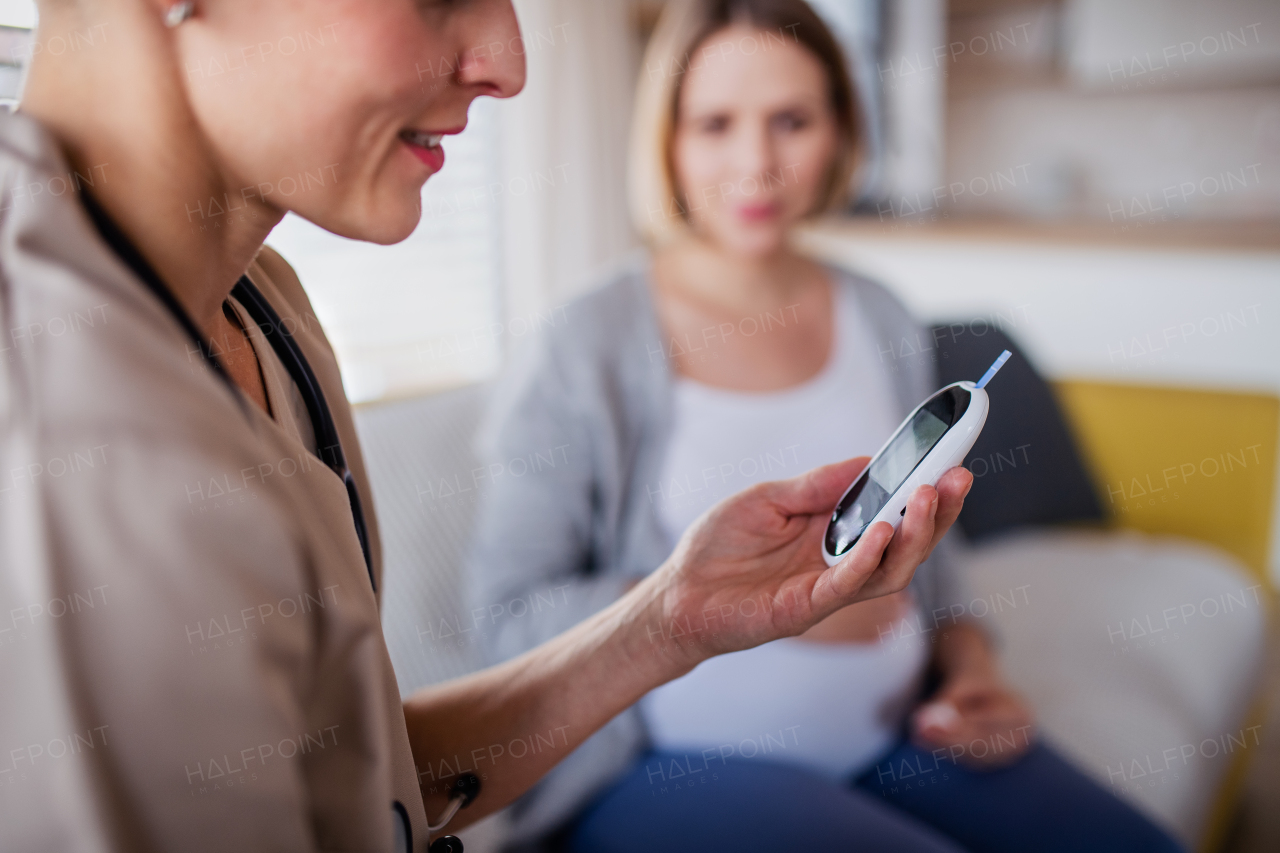 A healthcare worker examining pregnant woman indoors at home, checking blood sugar level for diabetes.