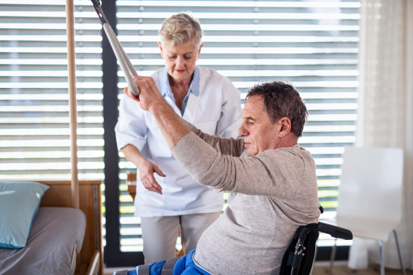 A healthcare worker helping paralysed senior patient in wheelchair in hospital.