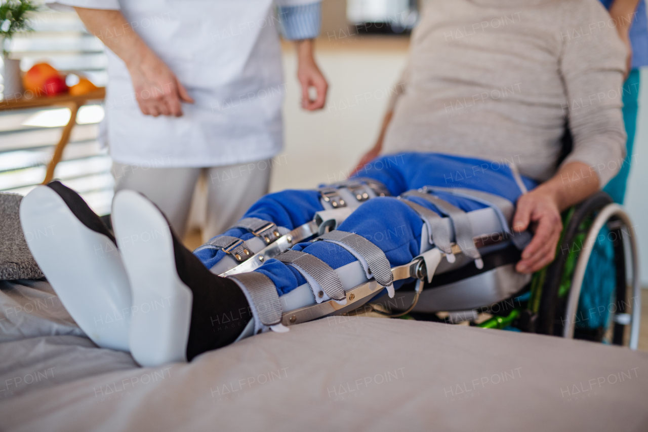 Unrecognizable healthcare worker and man paralysed senior patient with wheelchair and orthosis in hospital.