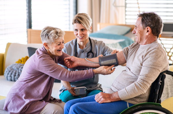 A healthcare worker visiting senior patient in wheelchair at home, blood pressure checking.