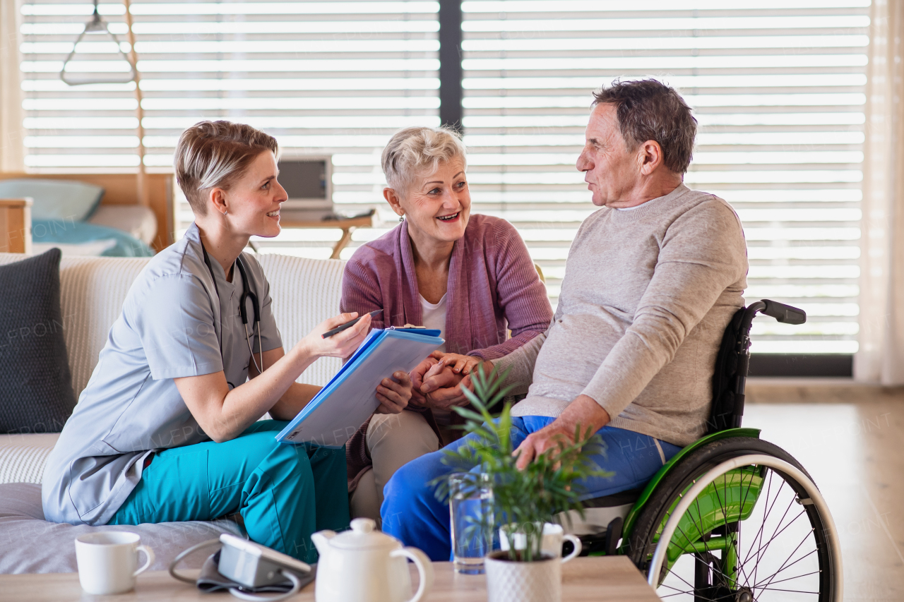 A healthcare worker visiting senior patient in wheelchair at home, talking.