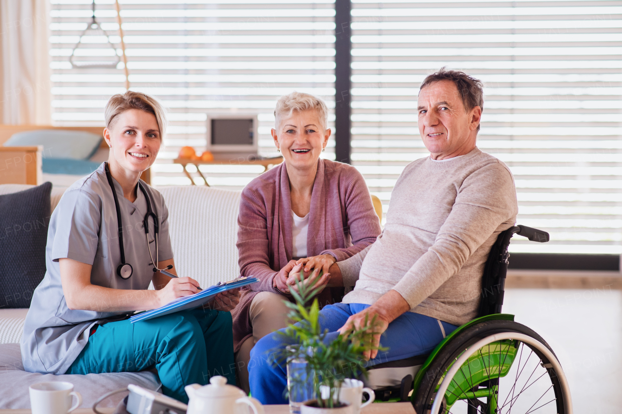 A healthcare worker visiting senior patient in wheelchair at home, looking at camera.