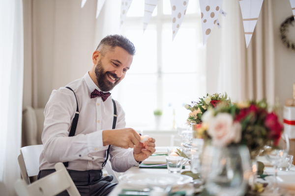 A portrait of hipster mature man indoors in a room set for a party, lighting candles.