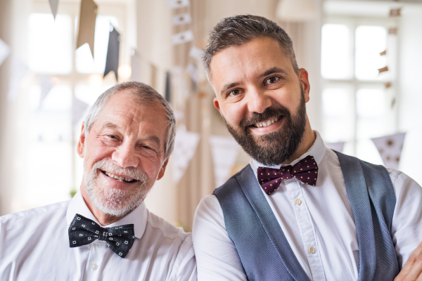 A portrait of a senior and hipster mature man standing indoors in a room set for a party, looking at the camera.