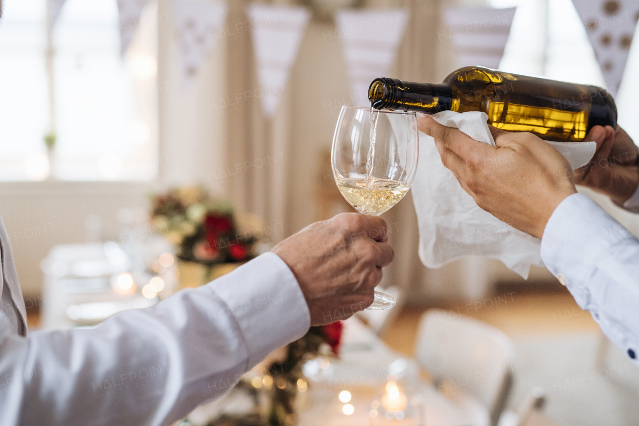 A midsection of unrecognizable man pouring happy guests wine on a indoor family birthday party.