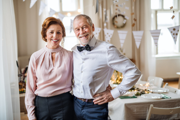 A portrait of a senior couple standing indoors in a room set for a party. Copy space.