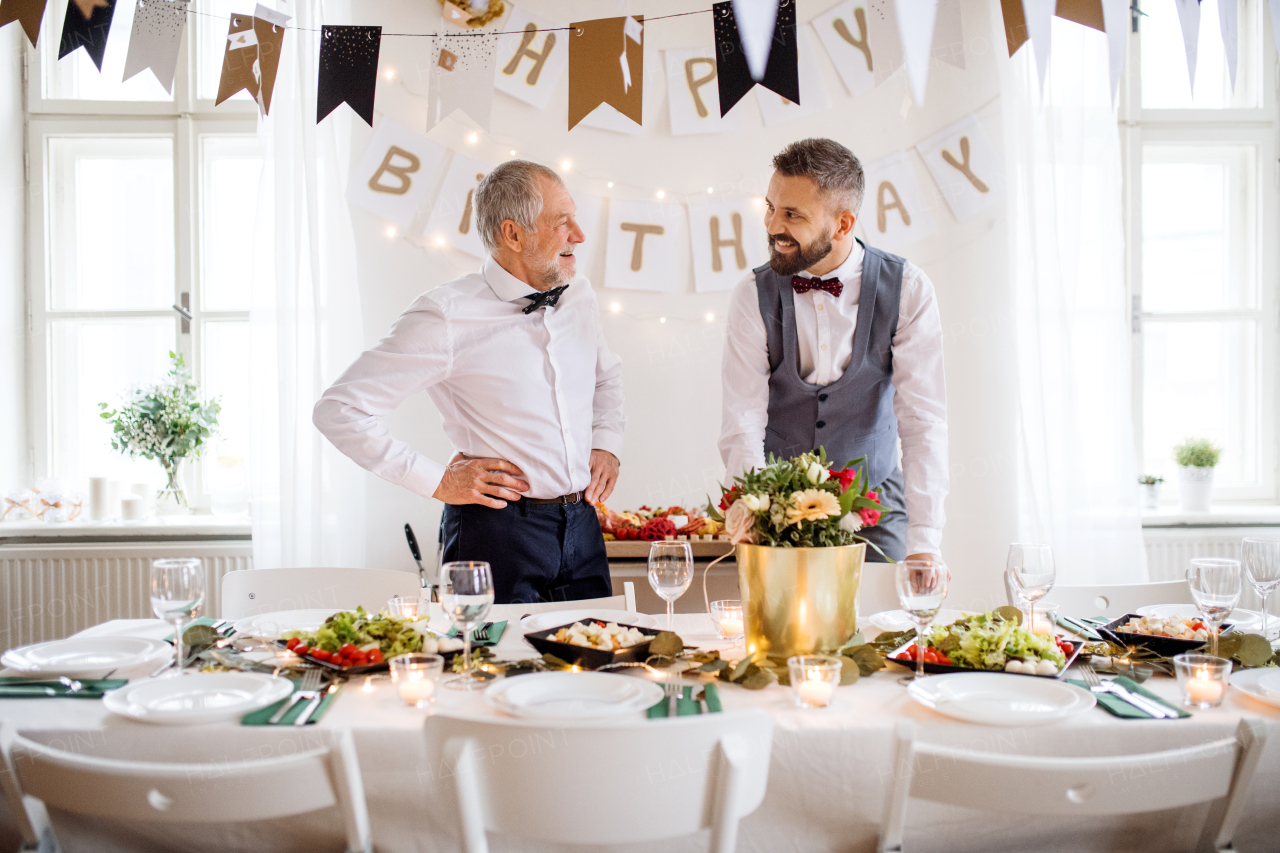 A portrait of a senior and hipster mature man standing indoors in a room set for a party, talking.