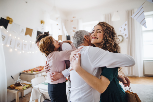 A young couple greeting parents or grandparents on indoor birthday party, hugging.