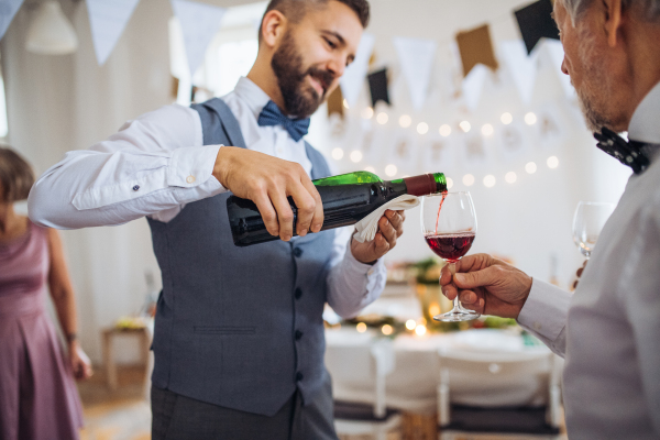 A man pouring happy guests wine on a indoor family birthday party.