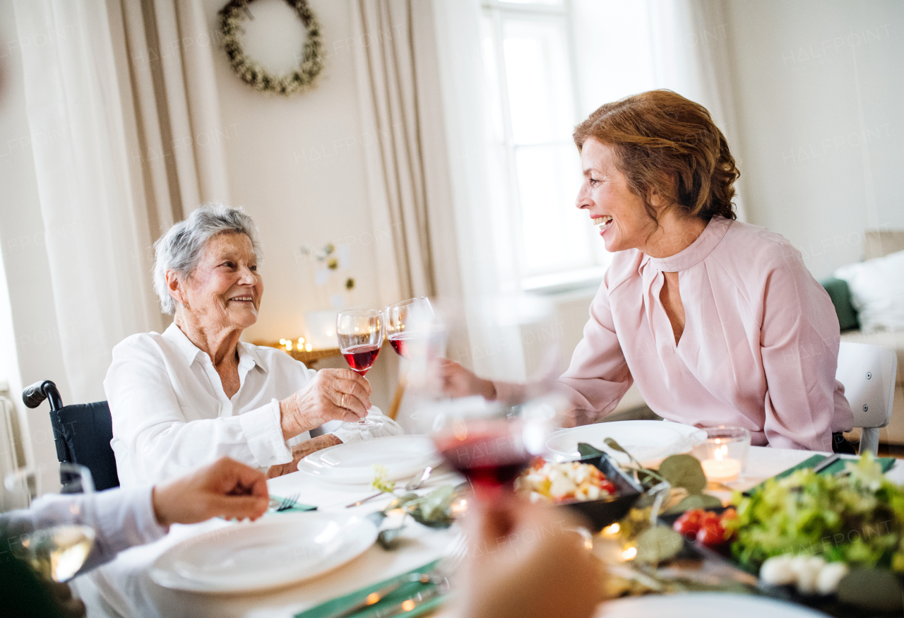 An elderly woman in wheelchair sitting at the table on a indoor birthday party, clinking glasses.