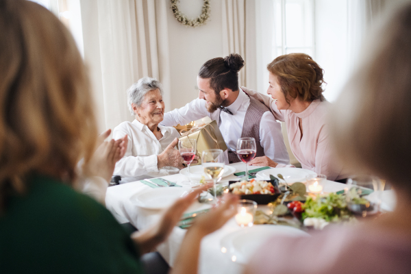 An elderly grandmother celebrating birthday with family and recieving a gift box, a party concept.