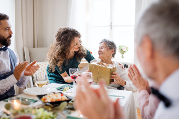 An elderly grandmother celebrating birthday with family and recieving a gift box, a party concept.