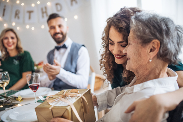 An elderly grandmother celebrating birthday with family and receiving a gift box, a party concept.