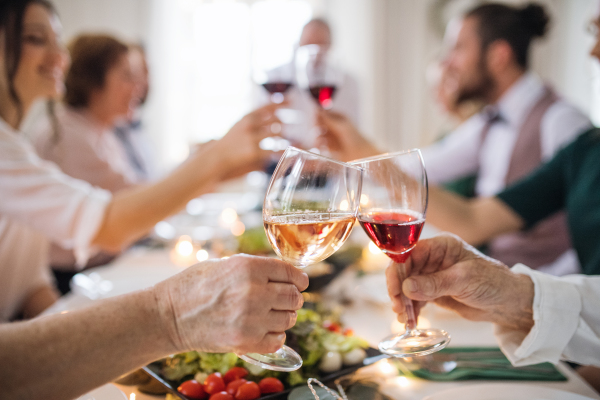 A midsection of big big family or friends sitting at a table on a indoor birthday party, clinking glasses.