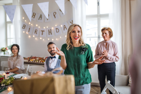 Happy surprised young woman receiving a gift on indoor party.