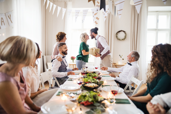 A man giving gift box to a young surprised woman on a family birthday party.