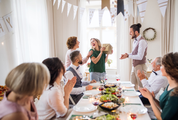 A man giving gift box to a young surprised woman on a family birthday party.