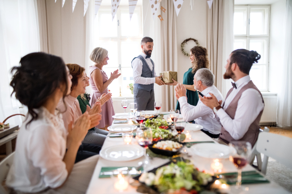 A man giving gift box to a young surprised woman on a family birthday or anniversary party.