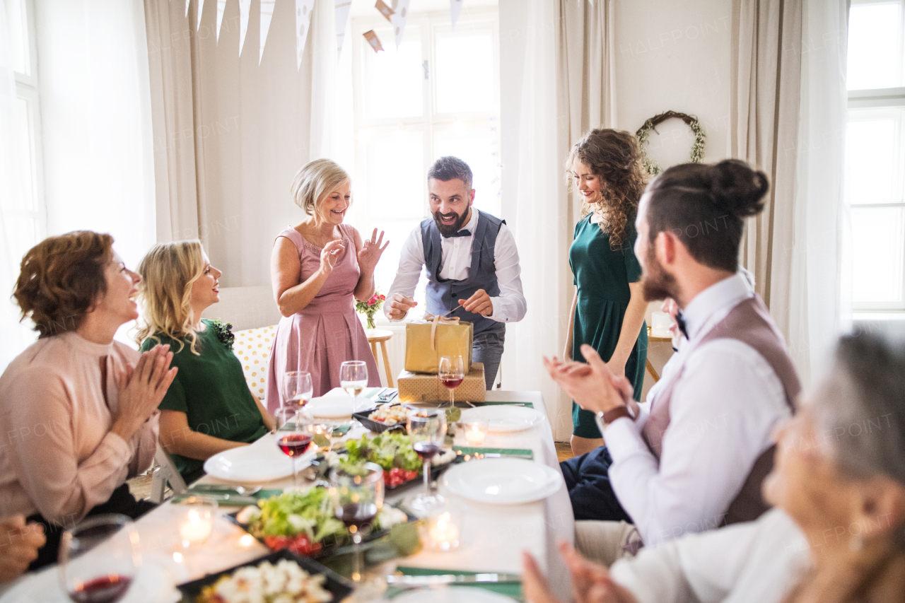 A happy mature man with friends and family opening presents on a birthday party.