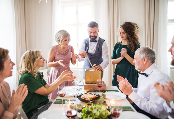 A happy mature man with friends and family opening presents on a birthday party.