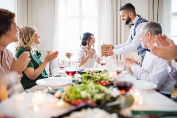 A man giving gift box to a young surprised woman on a family birthday or anniversary party.