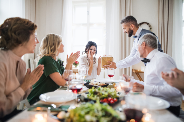 A man giving gift box to a young surprised woman on a family birthday or anniversary party.