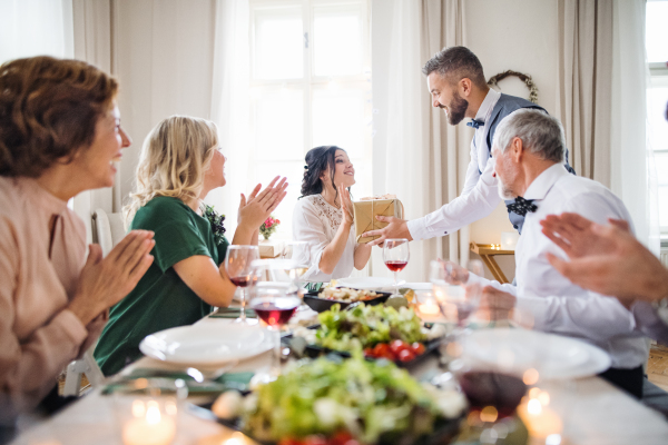 A man giving gift box to a young surprised woman on a family birthday or anniversary party.