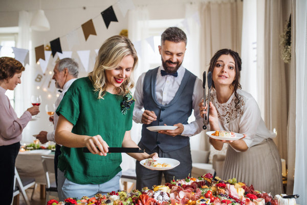 A multigeneration family putting food on plates on a indoor family birthday party.