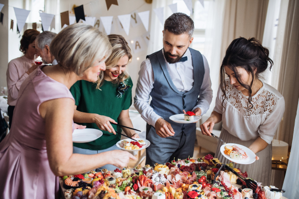 A multigeneration family putting food on plates on a indoor family birthday party.