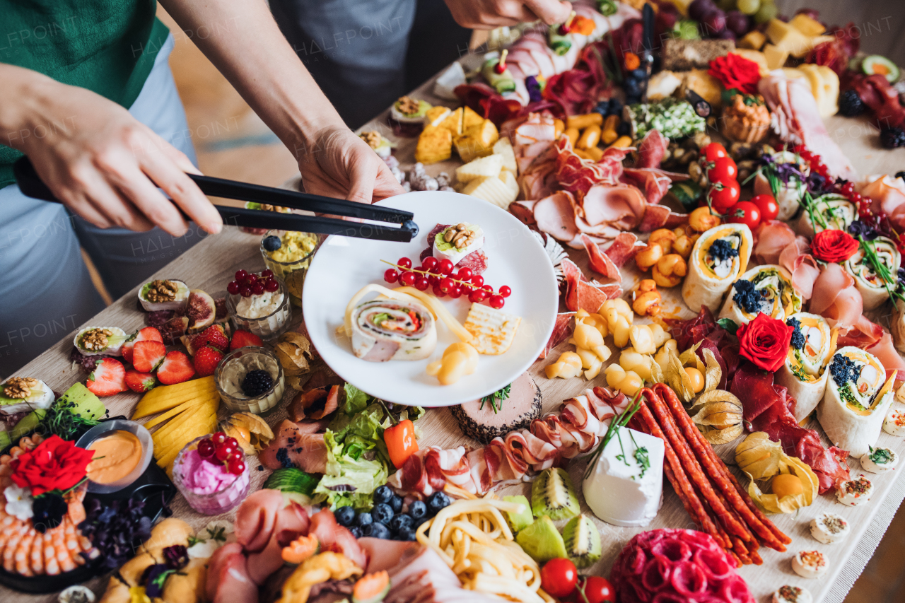 A top view of unrecognizable people putting food on plates on a indoor family birthday party.