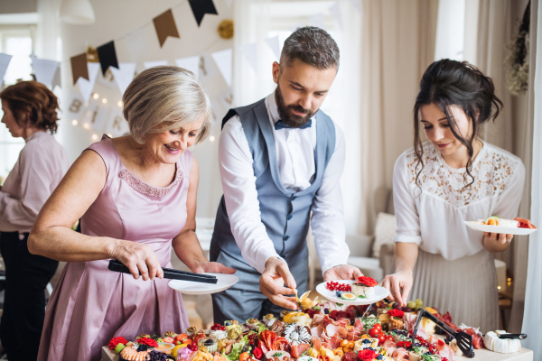 A multigeneration family putting food on plates on a indoor family birthday party.