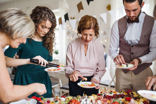 A multigeneration family putting food on plates on a indoor family birthday party.