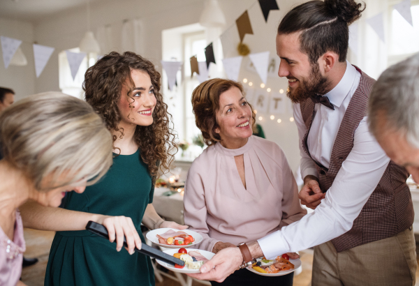 A multigeneration family putting food on plates on a indoor family birthday party.