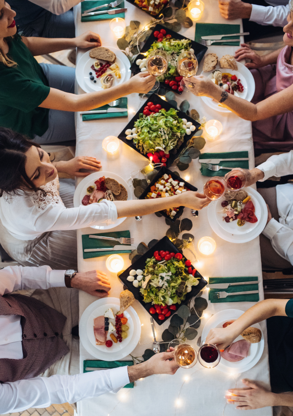 A top view of big family sitting at a table on a indoor birthday party, clinking glasses. A midsection.