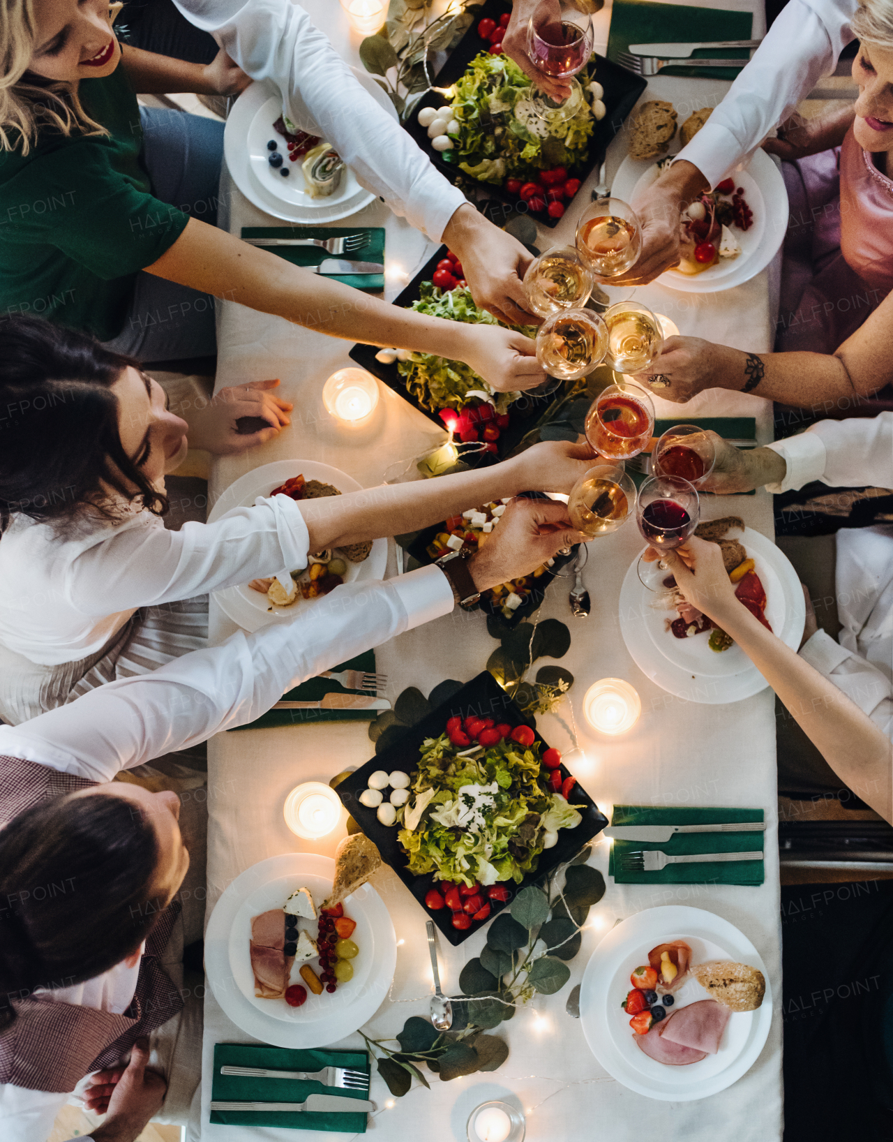 A midsection of big big family or friends sitting at a table on a indoor birthday party, clinking glasses. A top view.