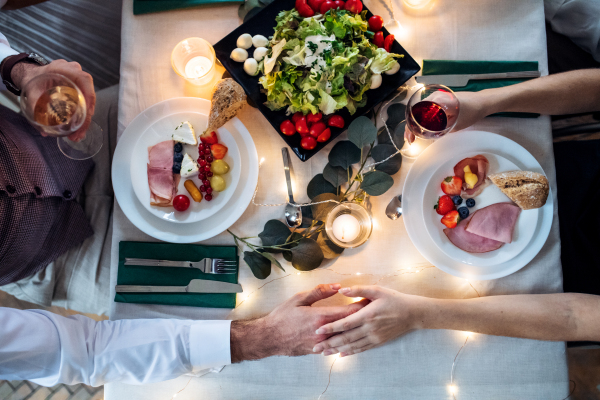 A top view of a couple in love sitting at a table on a indoor family party, holding glasses with wine.