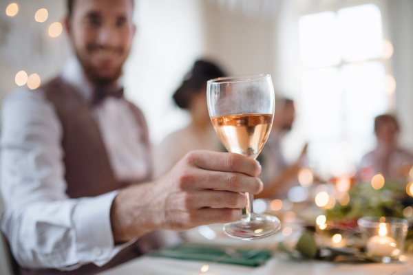 A close-up of male hand indoors in a room set for a party, holding a glass of white wine.